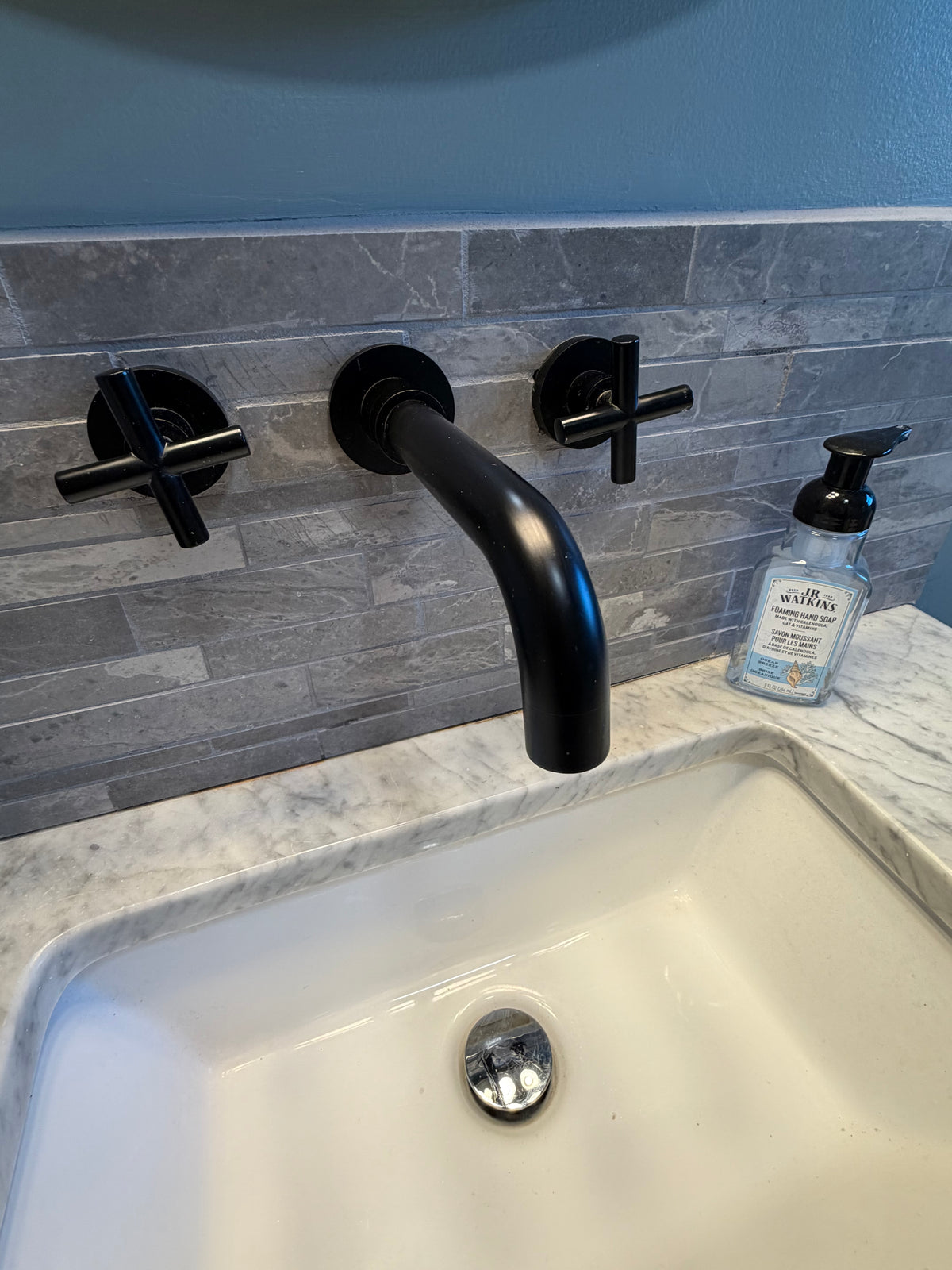 Matte black wall-mounted faucet with narrow vanity in blue guest bathroom